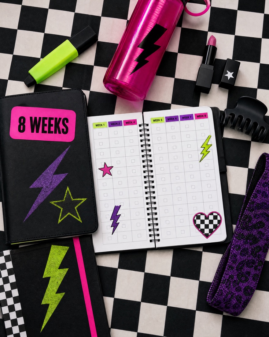 An 8-week planner on a checkerboard table with a highlighter, a water bottle, a lipstick and a hair clip